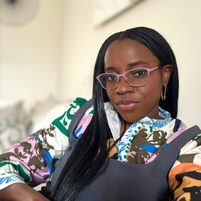 Former BellaNaija columnist Mrs Kush wearing pink glasses and a patterned top.