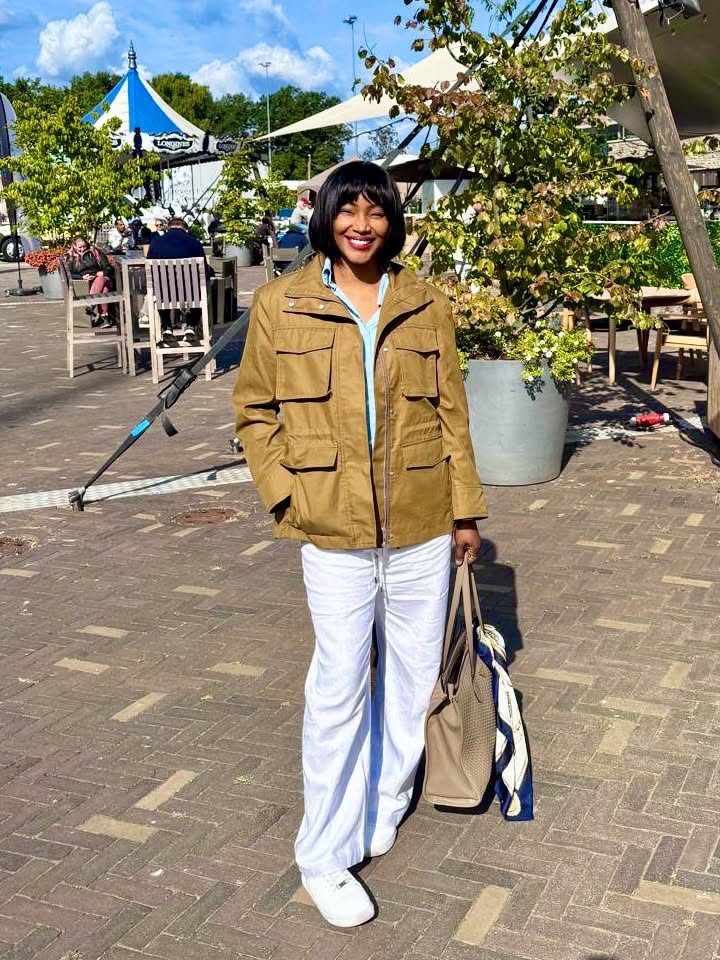 Isio Wanogho wearing a brown utility jacket, white trousers, and a short bob wig outdoors.