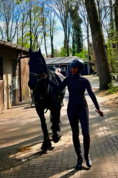 Former BellaNaija columnist Isio Wanogho leading a black horse in equestrian gear.