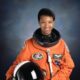 Dr Mae Jemison wearing an orange NASA Launch and Entry suit while holding her helmet.
