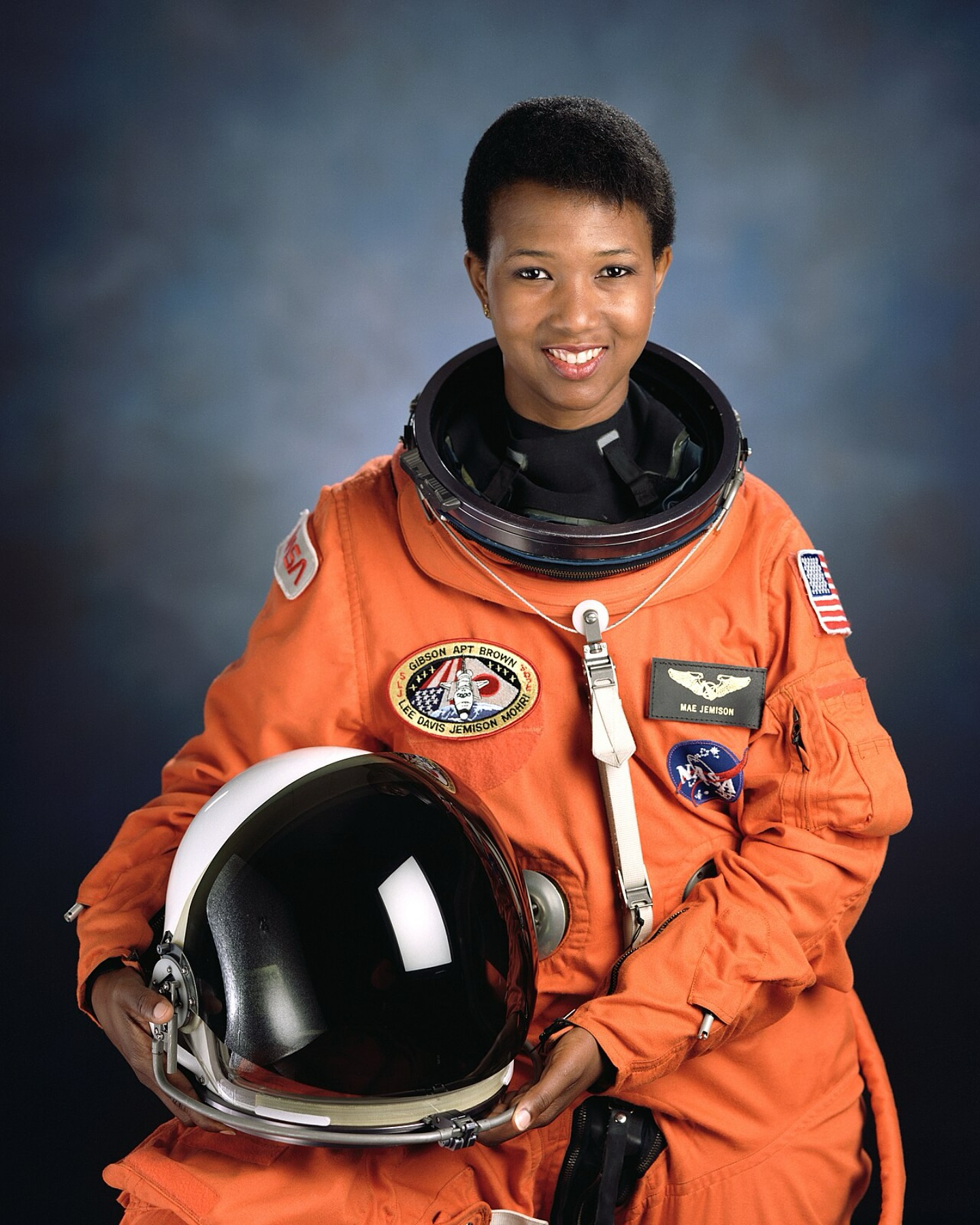 Dr Mae Jemison wearing an orange NASA Launch and Entry suit while holding her helmet.