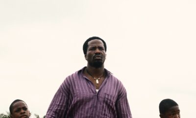British-Nigerian actor Ṣọpẹ́ Dìrísù as Folarin holding hands with young sons Remi and Akin on a dirt road in My Father’s Shadow.