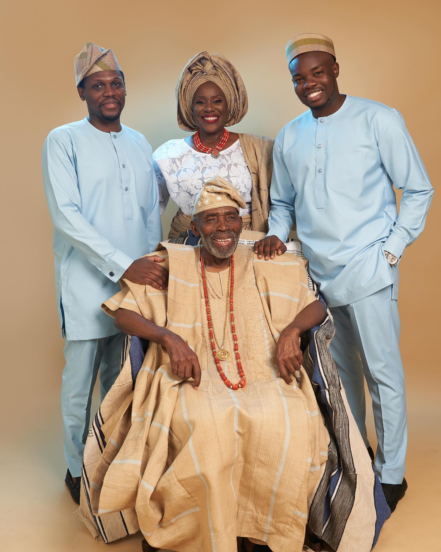 The late Olu Jacobs seated in beige traditional agbada surrounded by his wife Joke Silva and their sons.