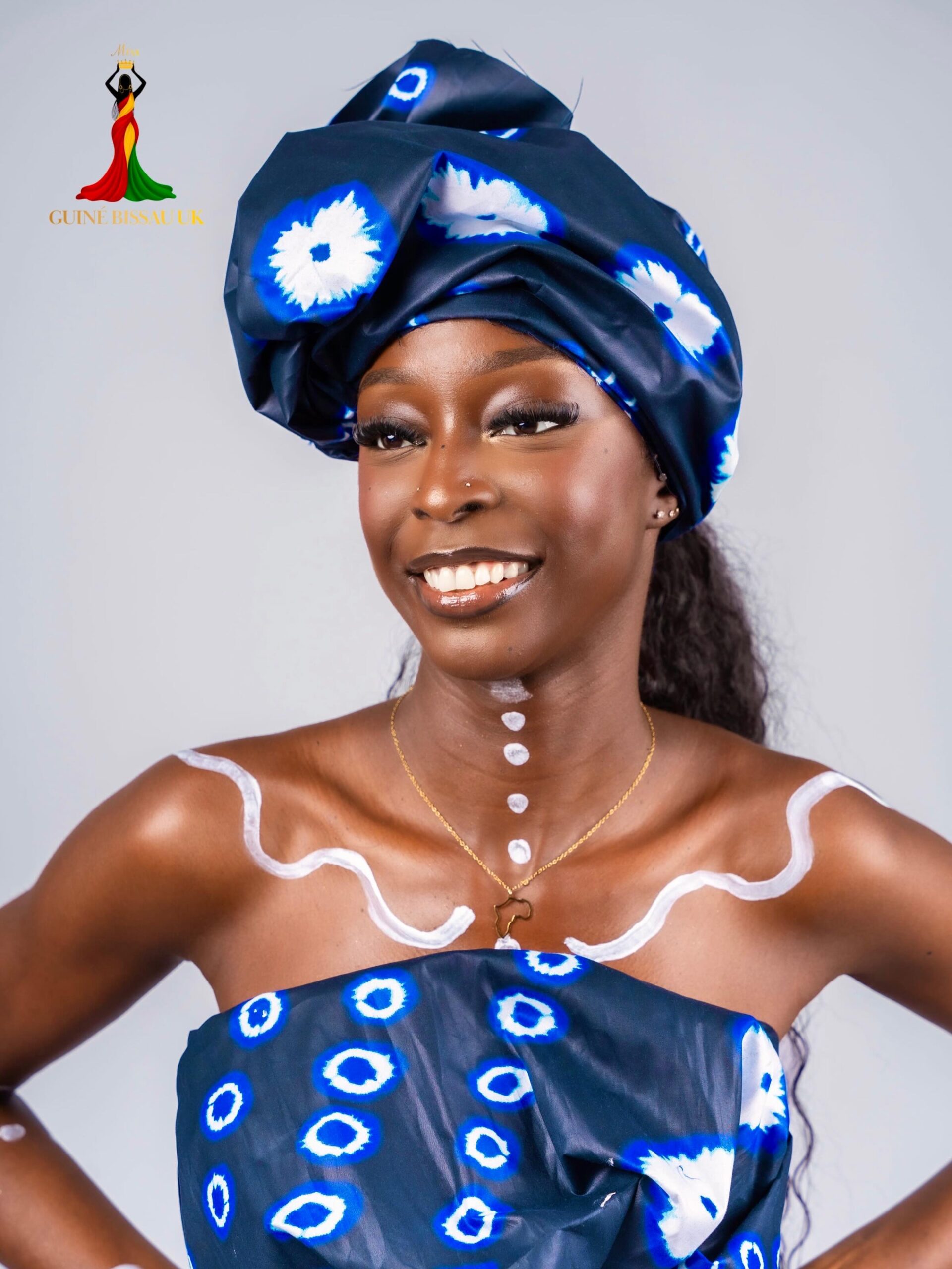 Ilce Dans smiling in a navy and white patterned headwrap and matching draped top for Miss Guiné-Bissau UK 2026