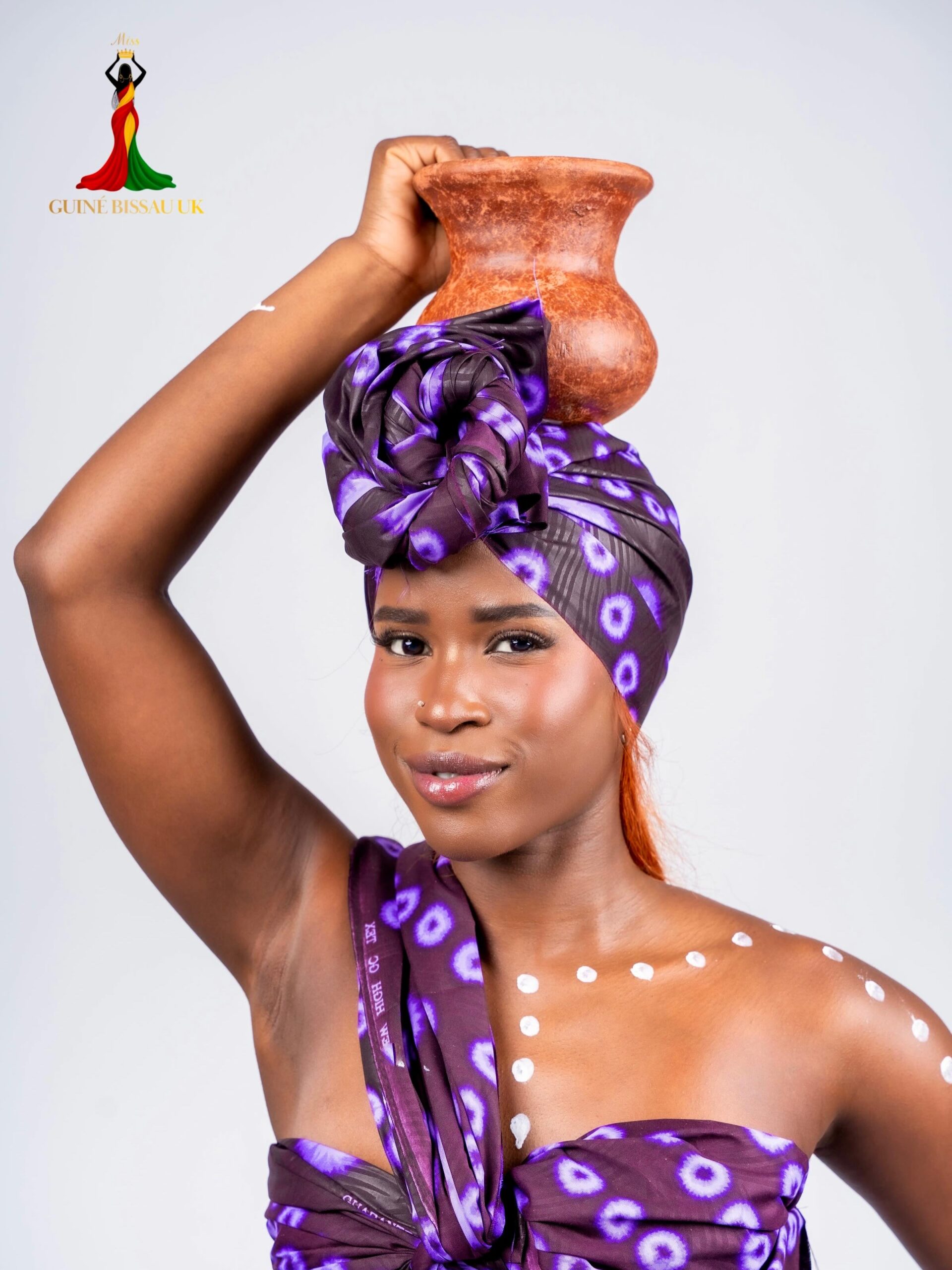 Vanessa Cassama holding a traditional clay pot while wearing a purple headwrap for Miss Guiné-Bissau UK 2026