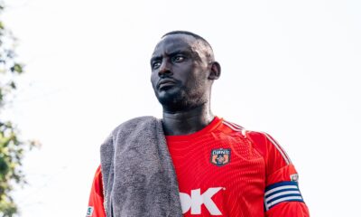 SE Dons captain George Desmond Kamurasi on the touchline wearing a red goalkeeper jersey and captain's armband.