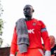 SE Dons captain George Desmond Kamurasi on the touchline wearing a red goalkeeper jersey and captain's armband.