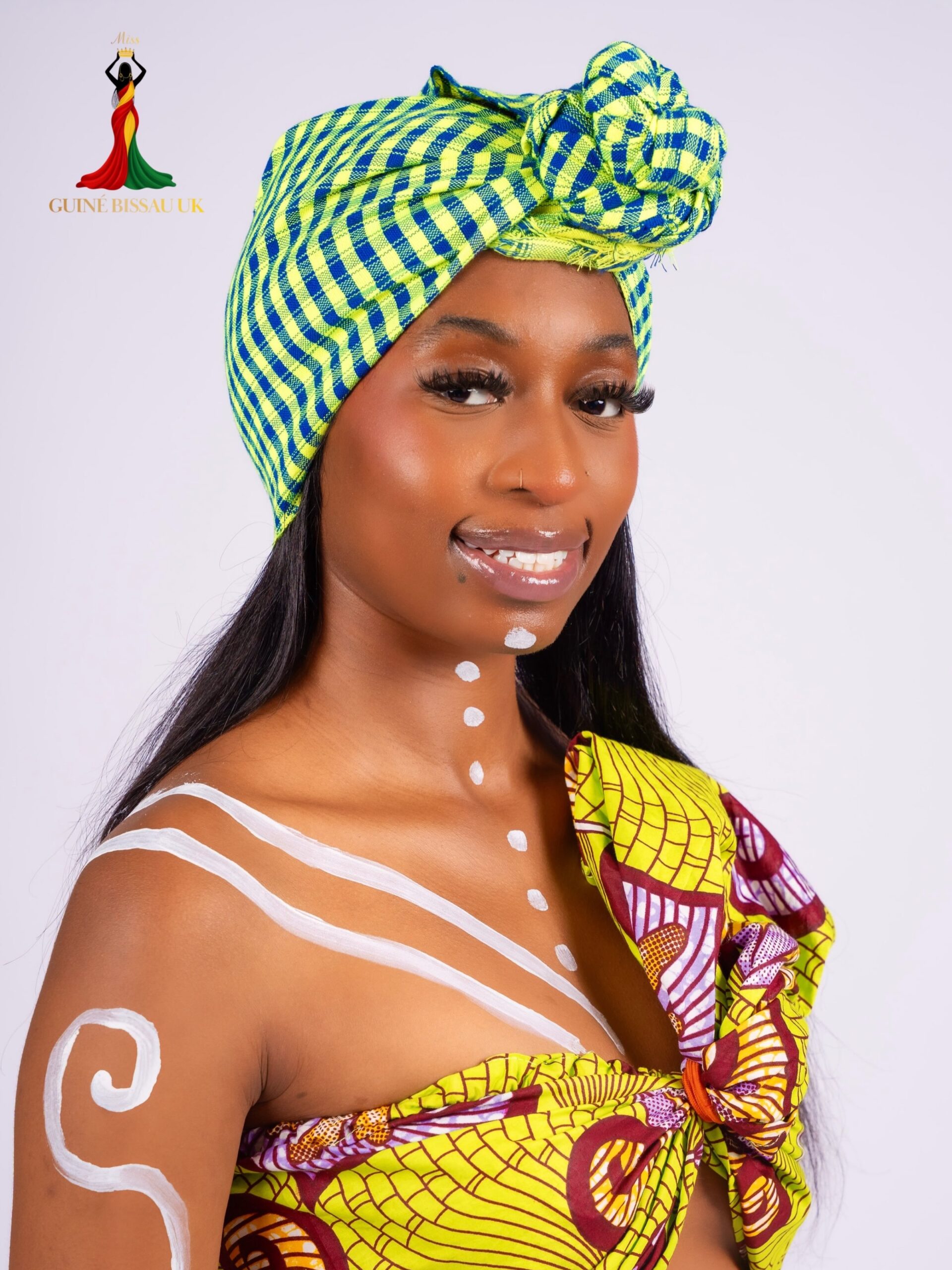 Manuela Cande Seidi smiling while wearing a lime green and blue checked headwrap with matching patterned outfit and white body paint for Miss Guiné-Bissau UK 2026
