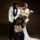 Laura Ajayi in a lace wedding gown and David Uruka in a white tuxedo standing behind Folagade Banks as Mama Deola
