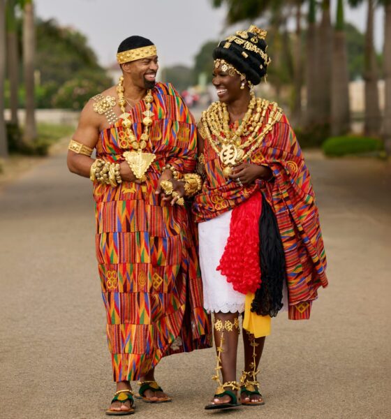 Bozoma Saint John and Keely Watson smiling at each other while walking in traditional hand-woven Kente drapes and gold jewellery.