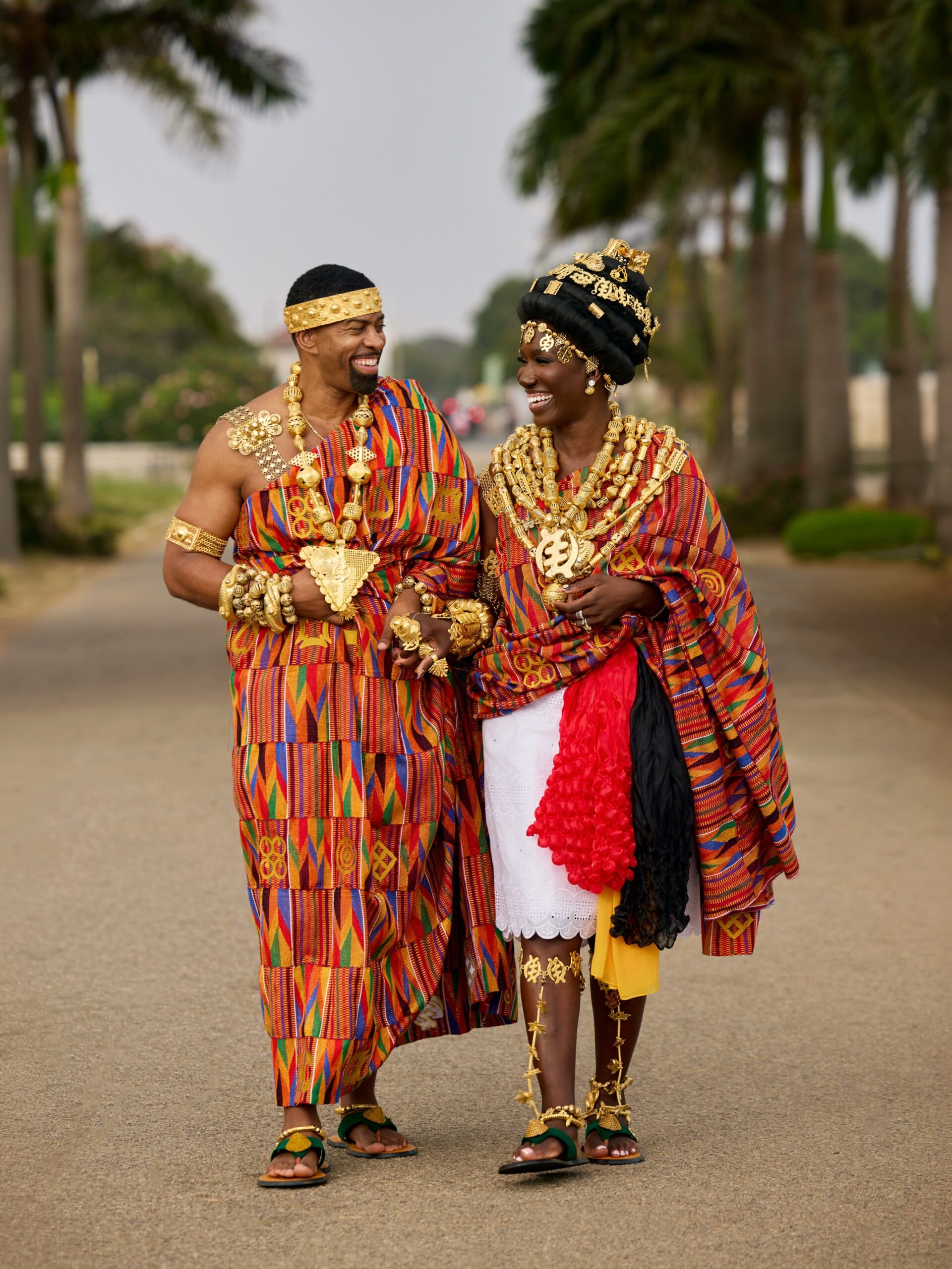 Bozoma Saint John and Keely Watson smiling at each other while walking in traditional hand-woven Kente drapes and gold jewellery.