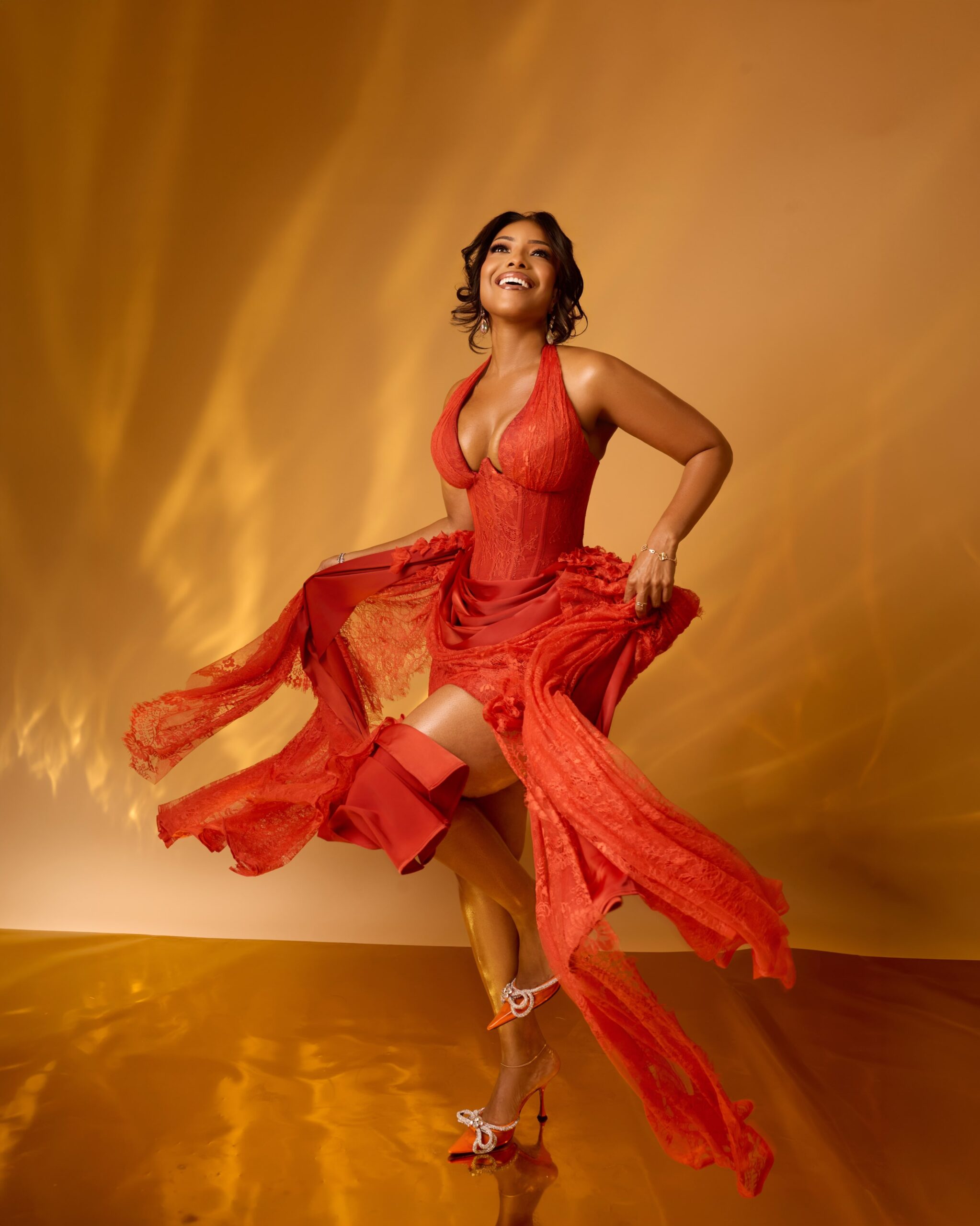Joselyn Dumas posing mid-motion in a red lace mini dress paired with embellished orange slingback heels