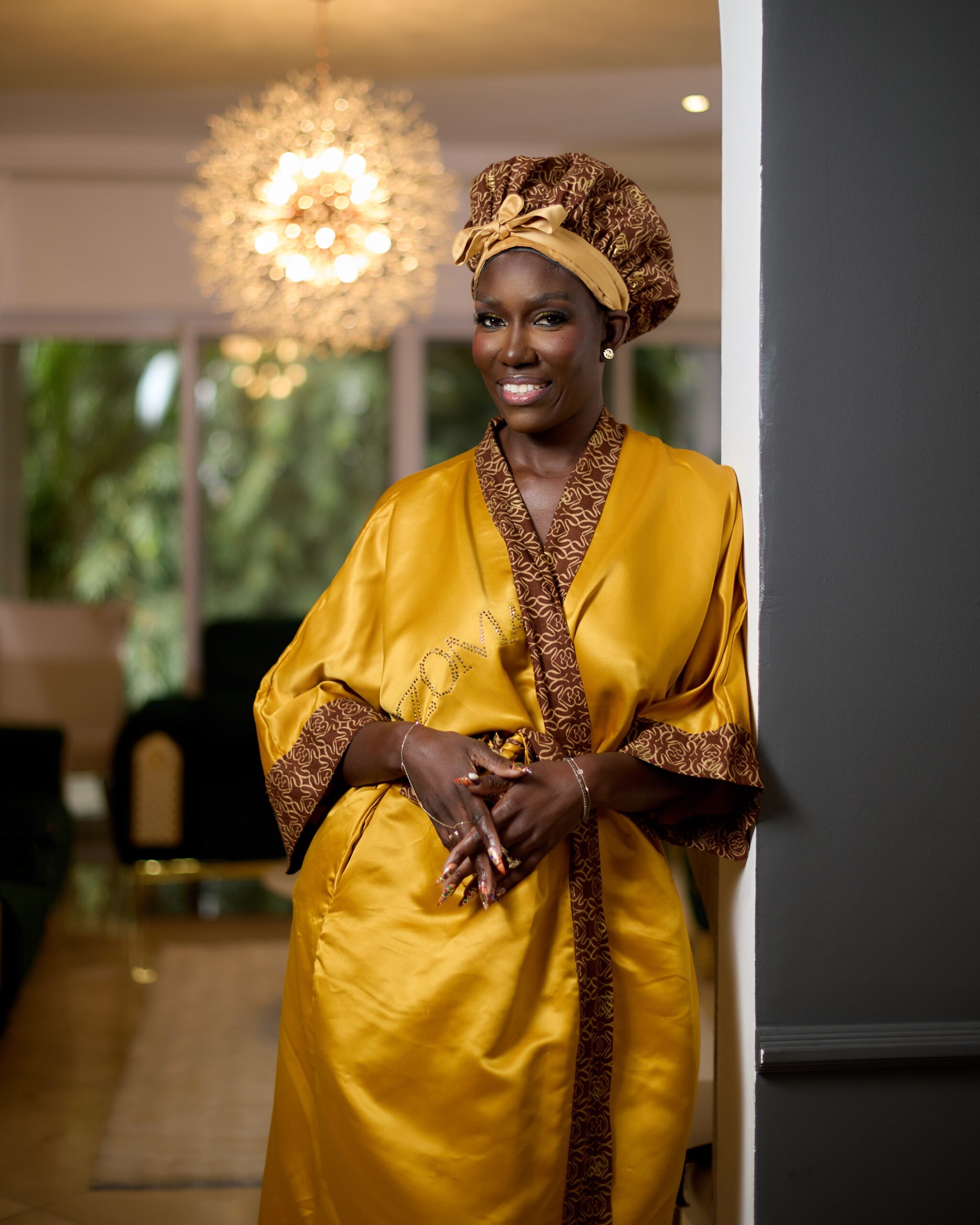 Bozoma Saint John smiling in a golden satin dressing gown and matching patterned bonnet during bridal preparations in Accra.