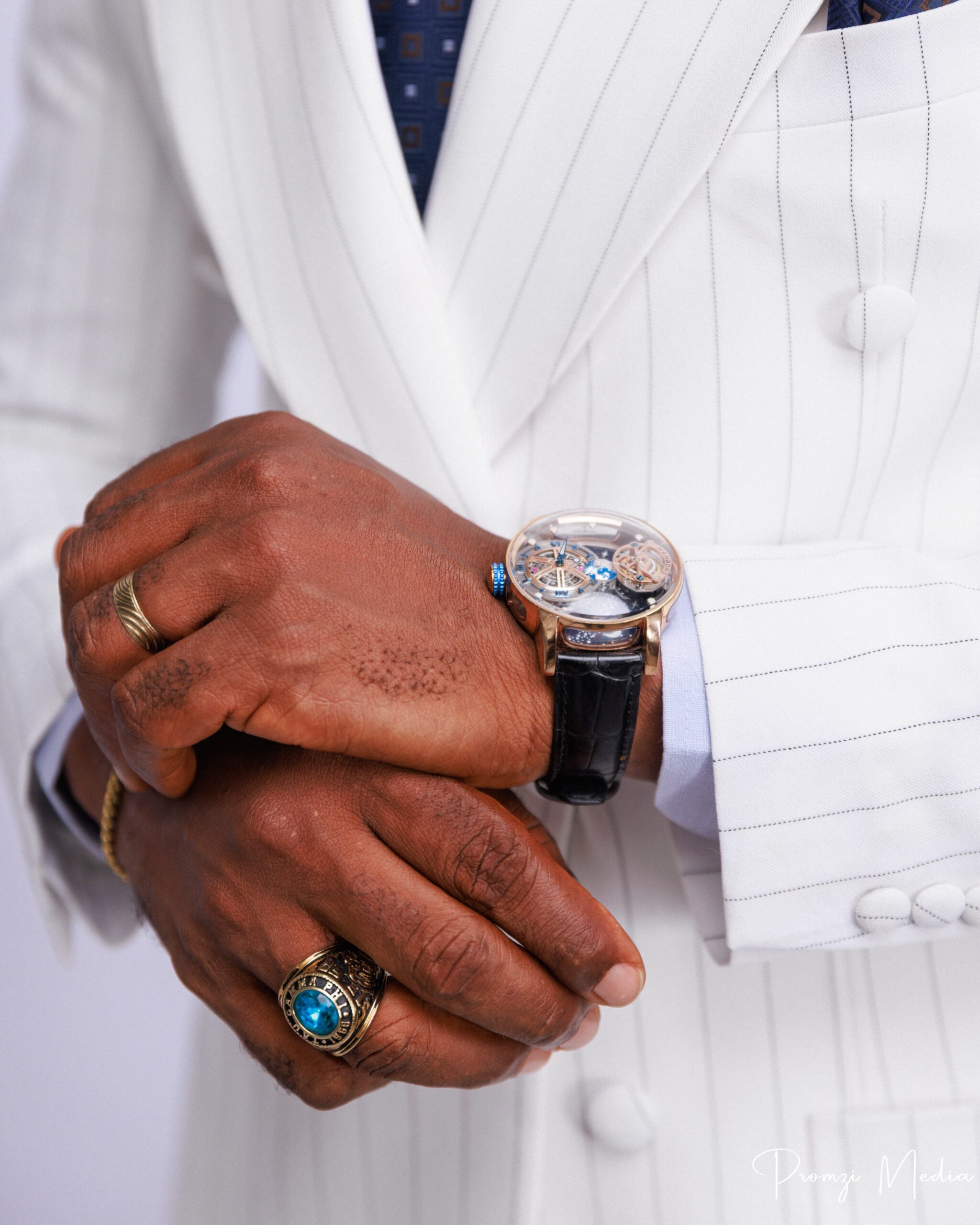 Lateef Adedimeji showing a luxury leather strap watch, gold signet ring, and pinstripe suit cuff
