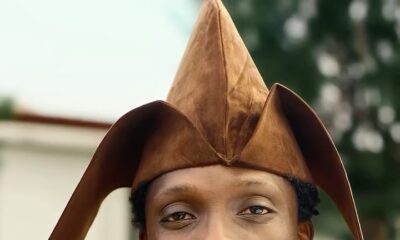 Afrogospel artist Greatman Takit wearing a brown Yoruba agbada, beaded neckpiece, and traditional fila cap on the set of his ADML music video.