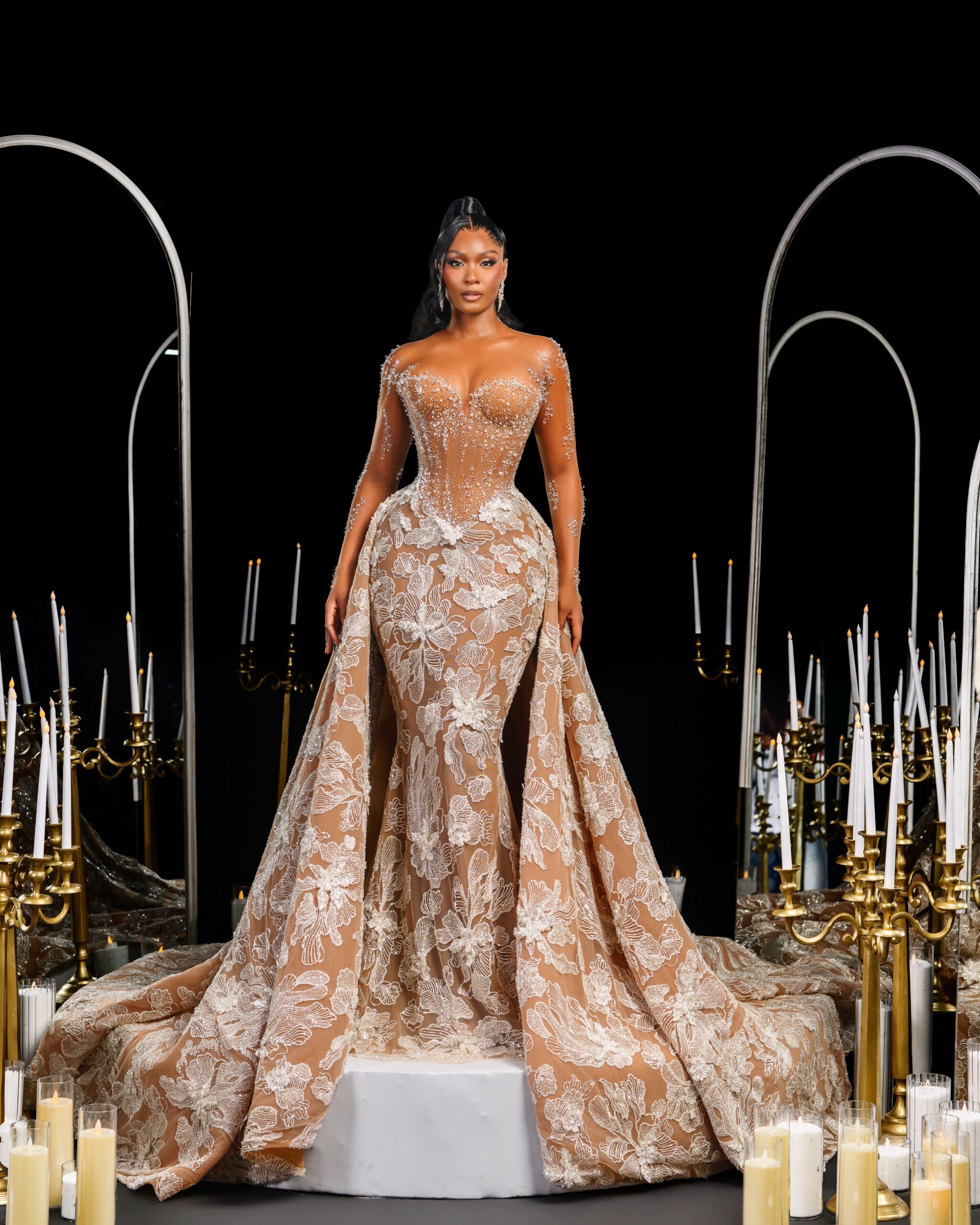 Osas Ighodaro standing on a stage in a custom sheer Veekee James lace gown with train