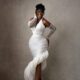 Hilda Baci smiling in a white pleated halterneck gown with pearl gloves and a vintage updo at A Mama Deola Wedding Story premiere.