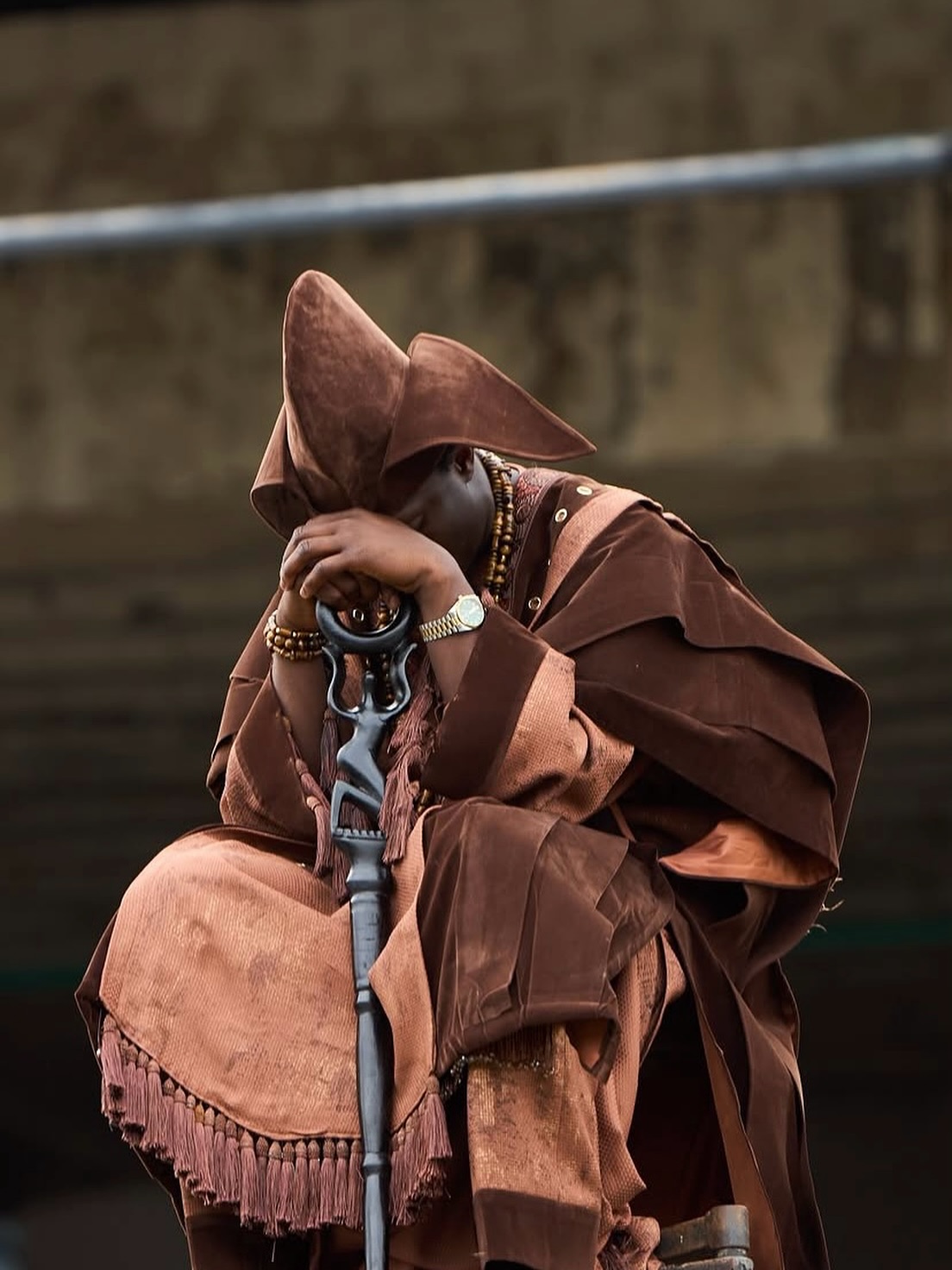 Greatman Takit resting his head on his hands over a carved wooden staff in a moment of prayer during the ADML video shoot.