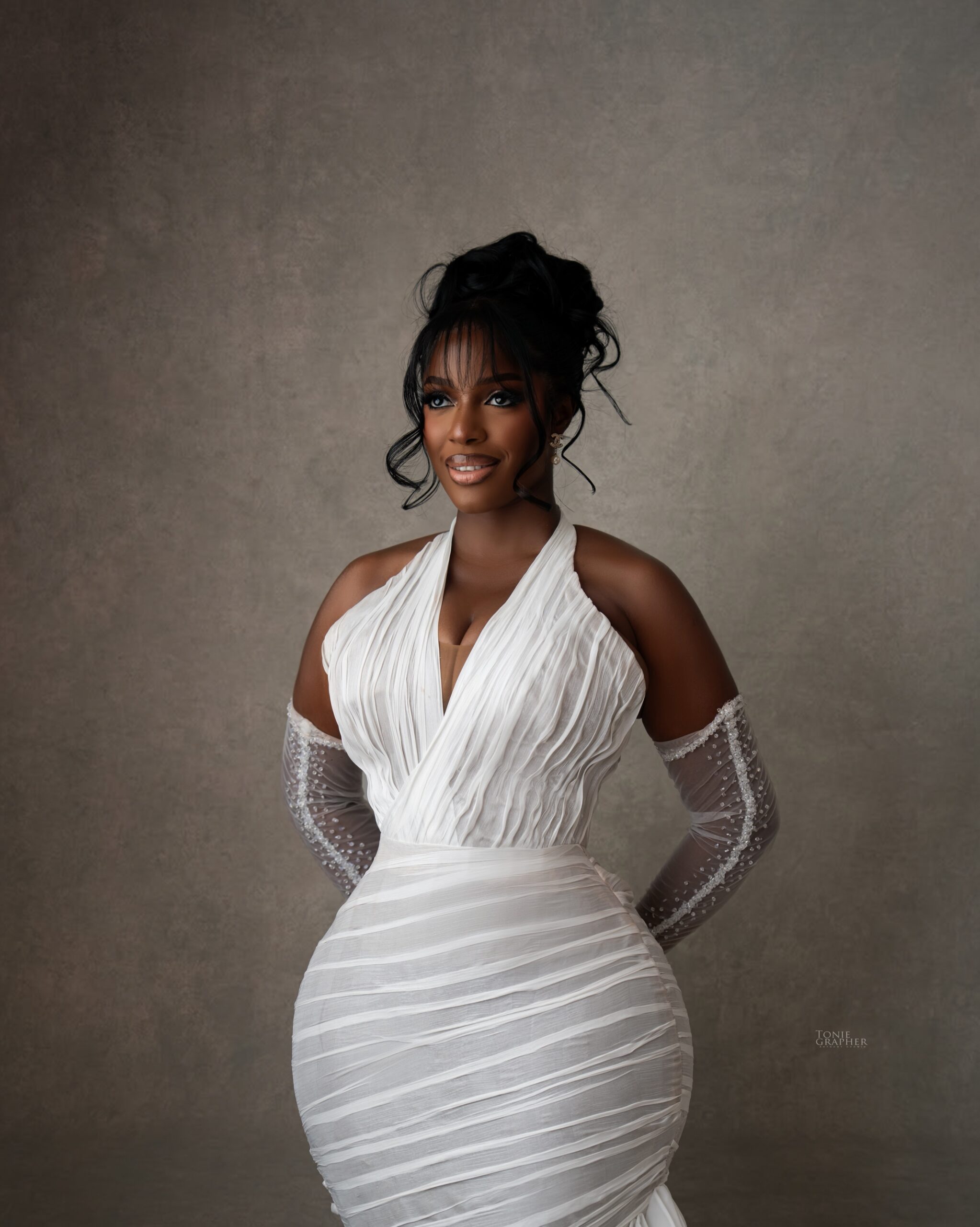 Hilda Baci in a white pleated halterneck gown with ruched waist detailing, sheer pearl gloves, and fringe bangs at A Mama Deola Wedding Story premiere.