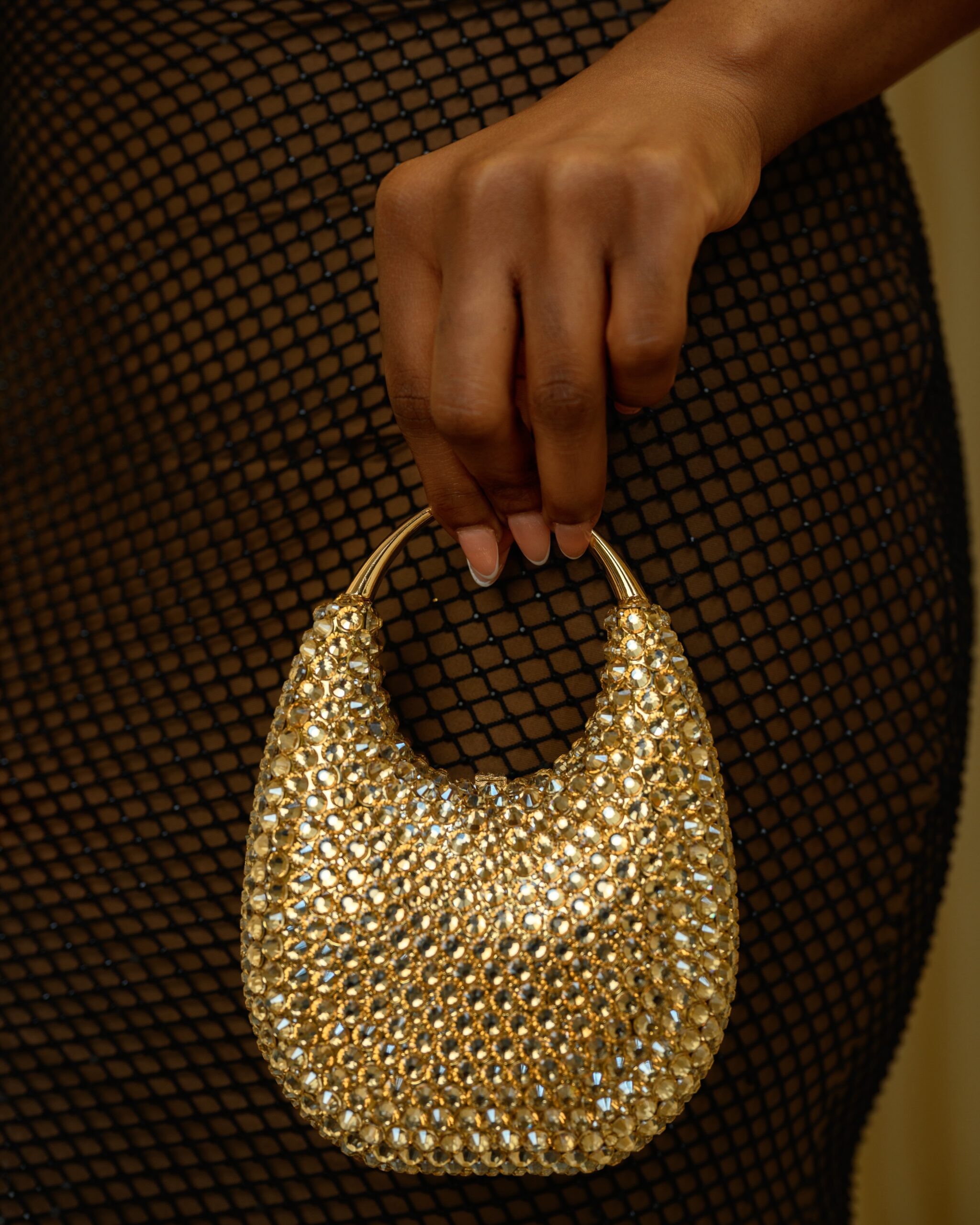 Gold pavé crystal micro handbag held against Bella Okagbue's black fishnet dress texture.