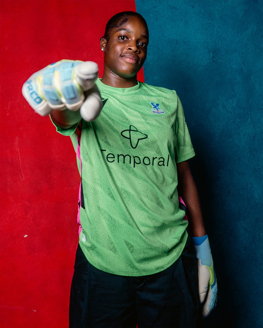 Comfort Erhabor wearing a green Crystal Palace goalkeeper kit pointing towards the camera with a gloved hand.