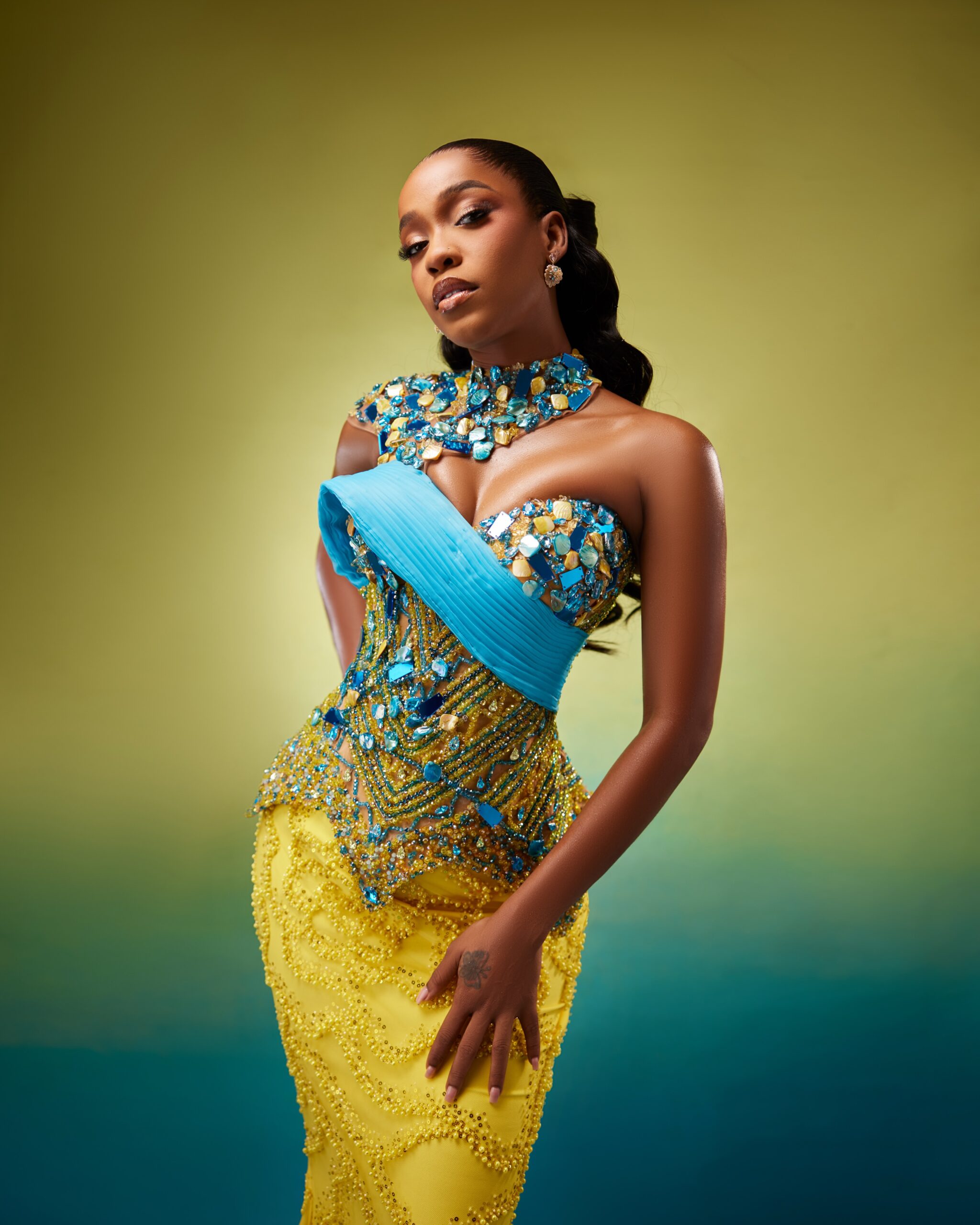 Efe Irele wearing a yellow beaded corset dress with blue stone embellishments and asymmetrical neckline.