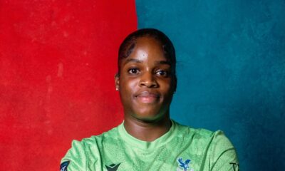 Comfort Erhabor sitting with arms crossed wearing a green Crystal Palace goalkeeper jersey and gloves.