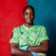 Comfort Erhabor sitting with arms crossed wearing a green Crystal Palace goalkeeper jersey and gloves.
