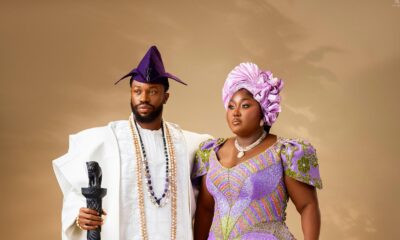 Stan Nze in a white embroidered Agbada holding a lion-head staff beside Blessing Nze in an ombré purple gown and lilac Gele.
