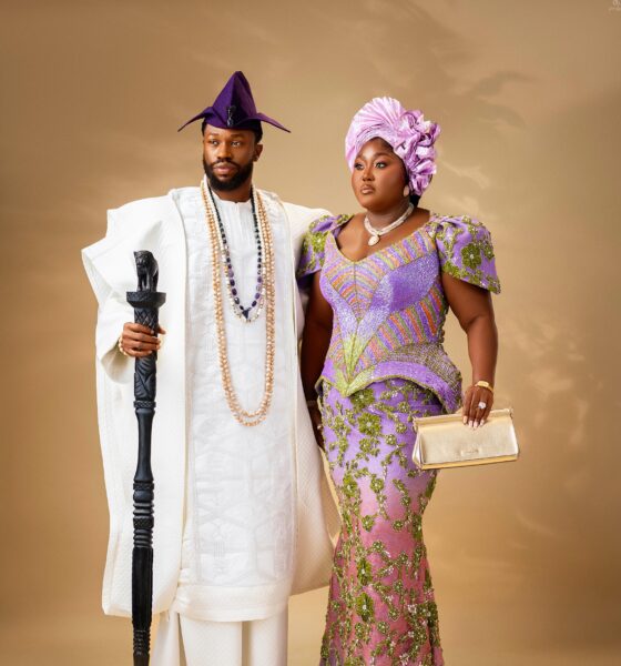 Stan Nze in a white embroidered Agbada holding a lion-head staff beside Blessing Nze in an ombré purple gown and lilac Gele.