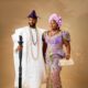 Stan Nze in a white embroidered Agbada holding a lion-head staff beside Blessing Nze in an ombré purple gown and lilac Gele.