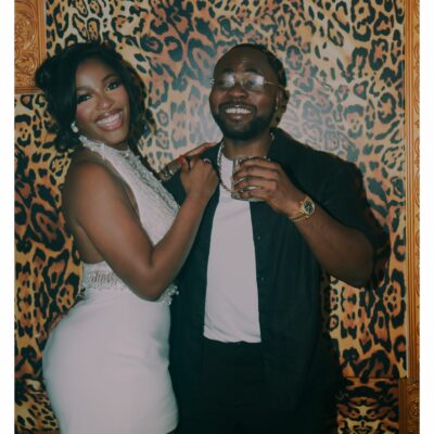 Hilda Baci wearing a white halter mini dress with beaded fringe beside partner Damilola Akinwunmi