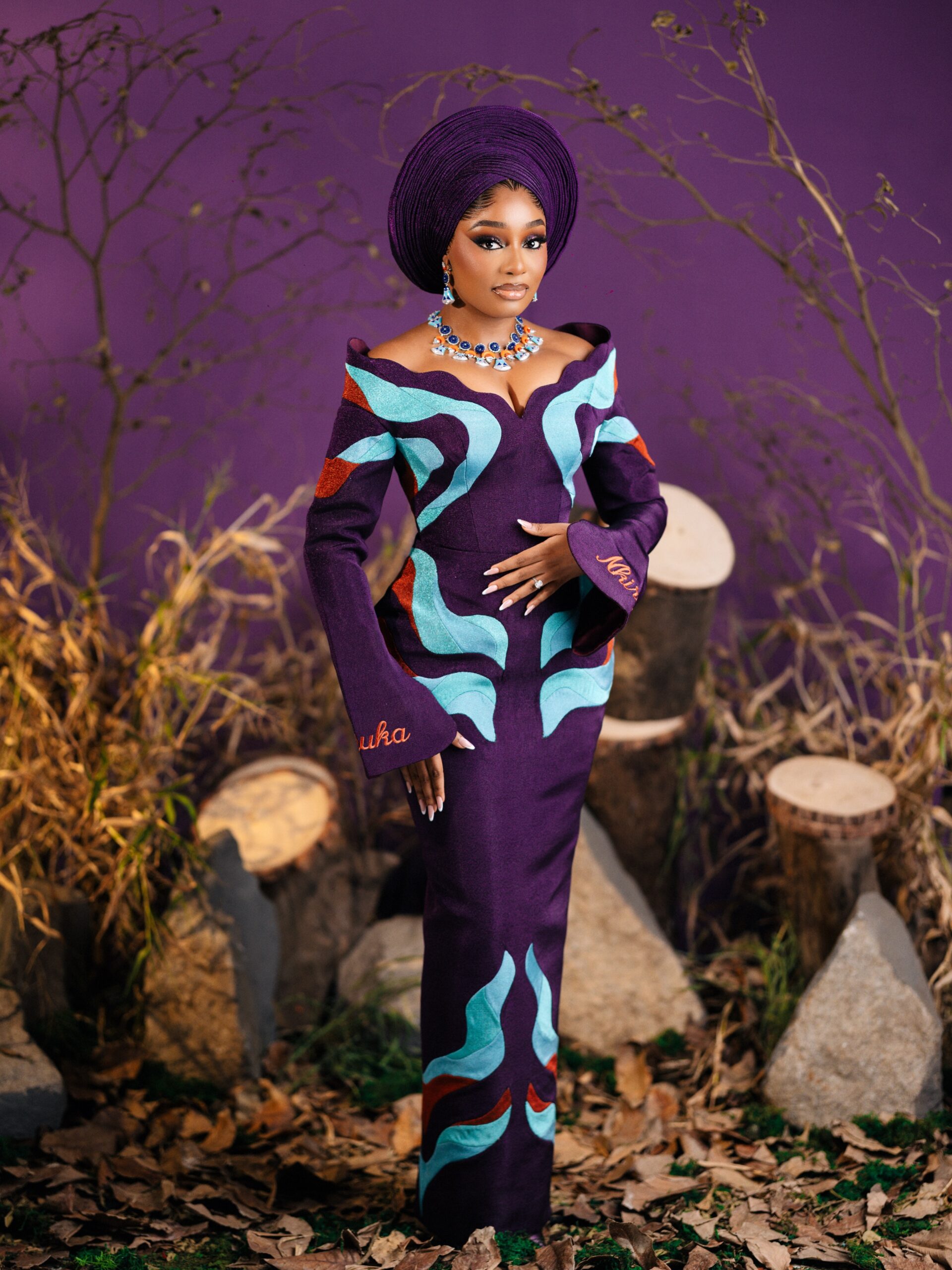 Kiky Festus in a deep purple off-the-shoulder Nichole Stylish gown with teal geometric appliqués and custom story beadwork.