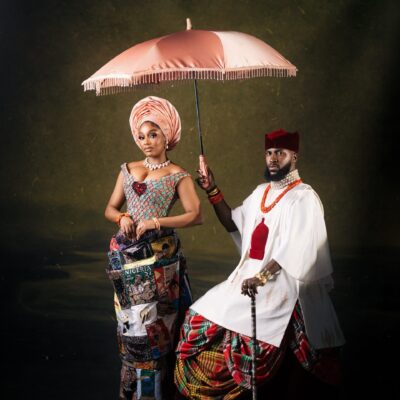 Kiky Festus under a pink parasol next to Akin Faminu in a white tunic and tartan George skirt.