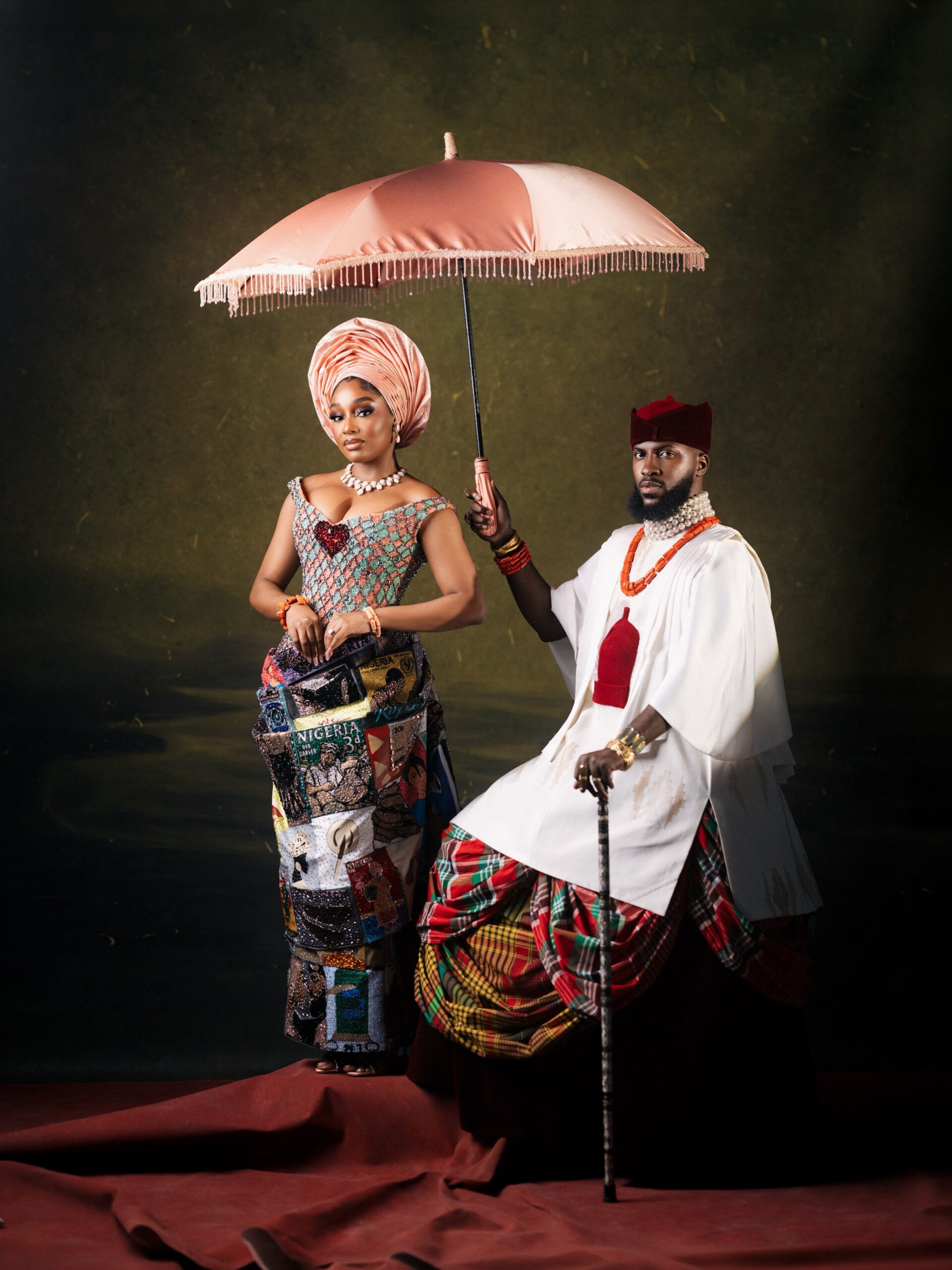 Kiky Festus under a pink parasol next to Akin Faminu in a white tunic and tartan George skirt.
