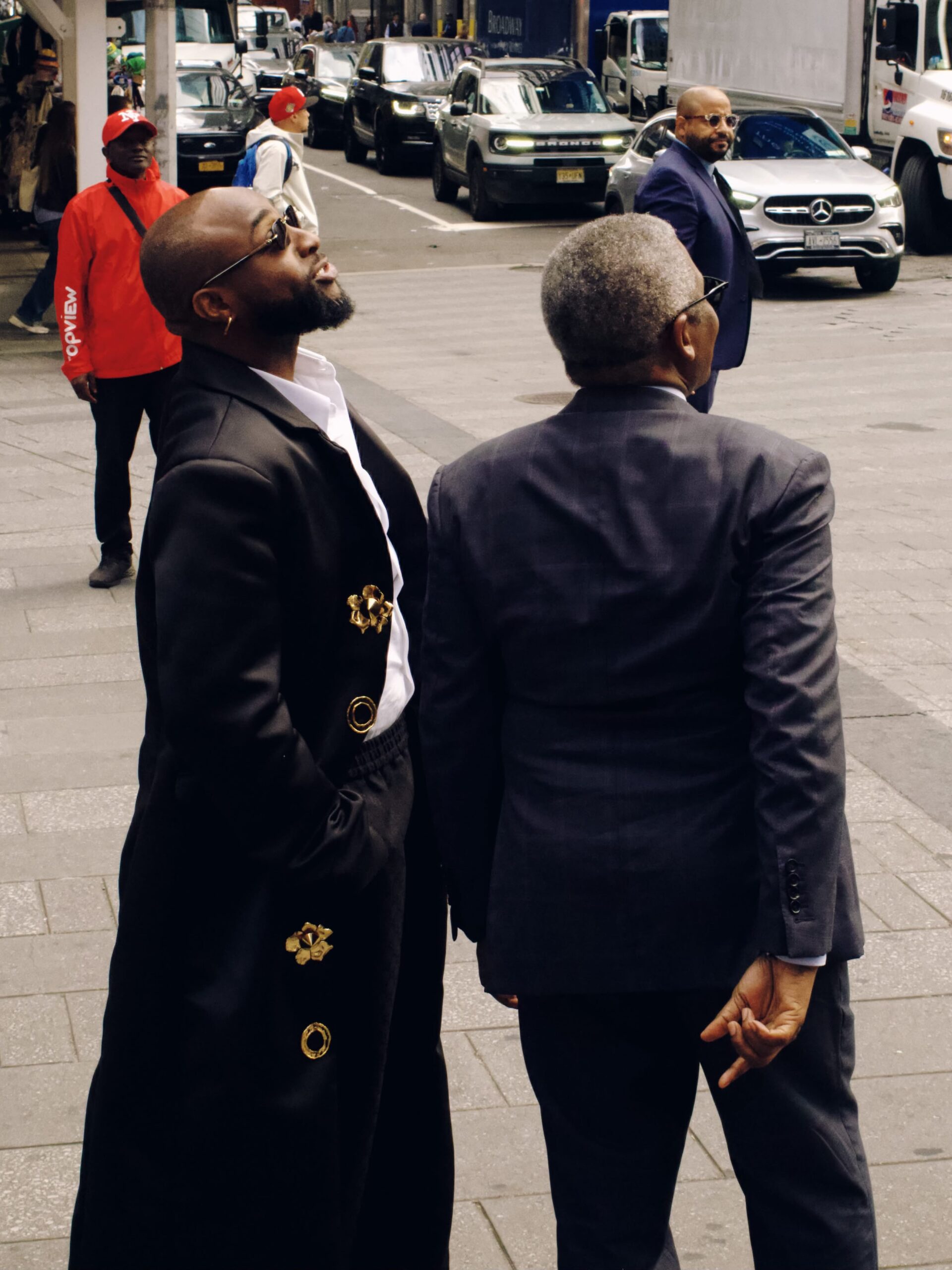 Davido and Aliko Dangote looking up toward the Dangote Refinery advertisement in Times Square