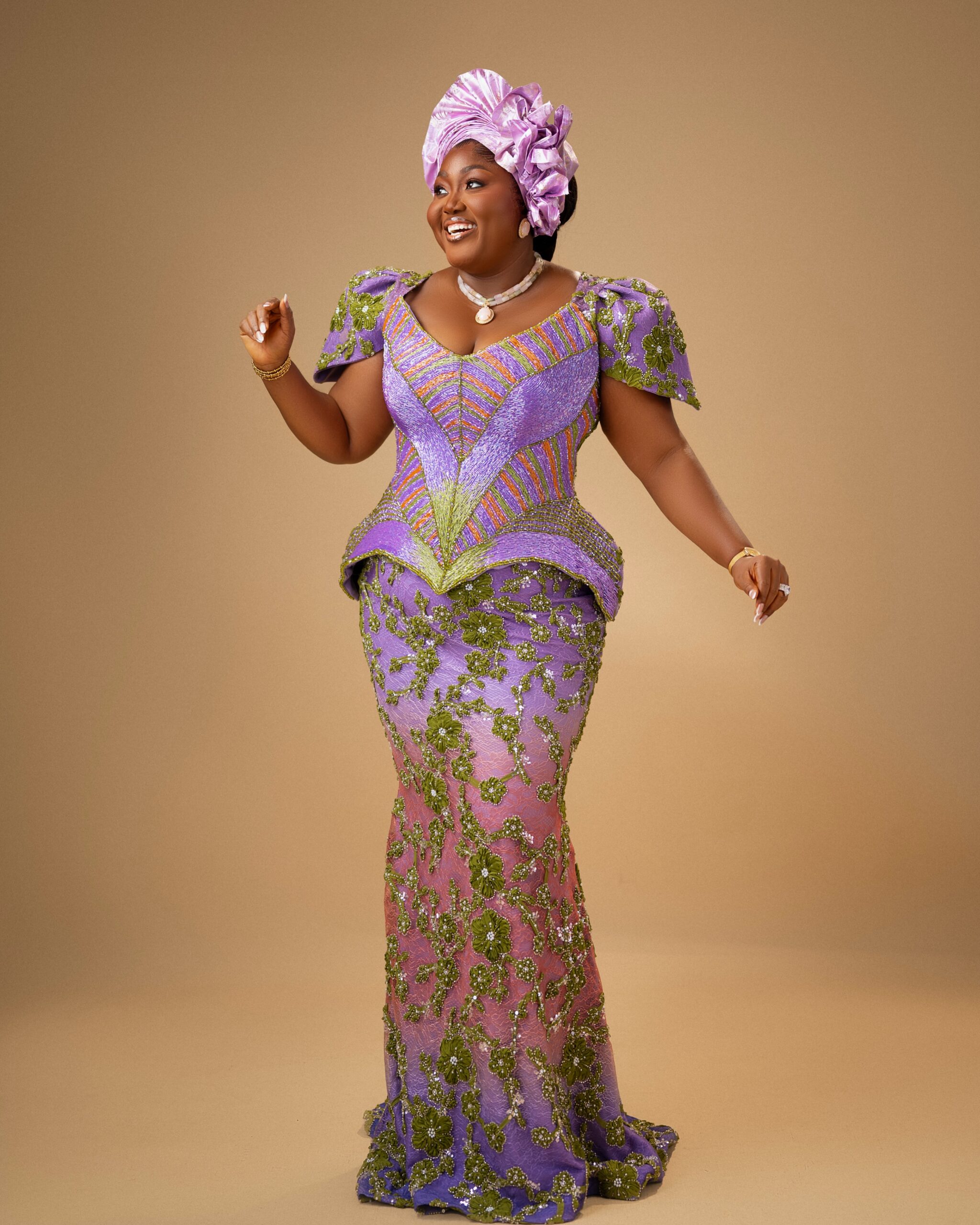 Blessing Nze displaying her full-length ombré purple and mauve traditional lace gown with green floral embroidery and structured peplum waist.