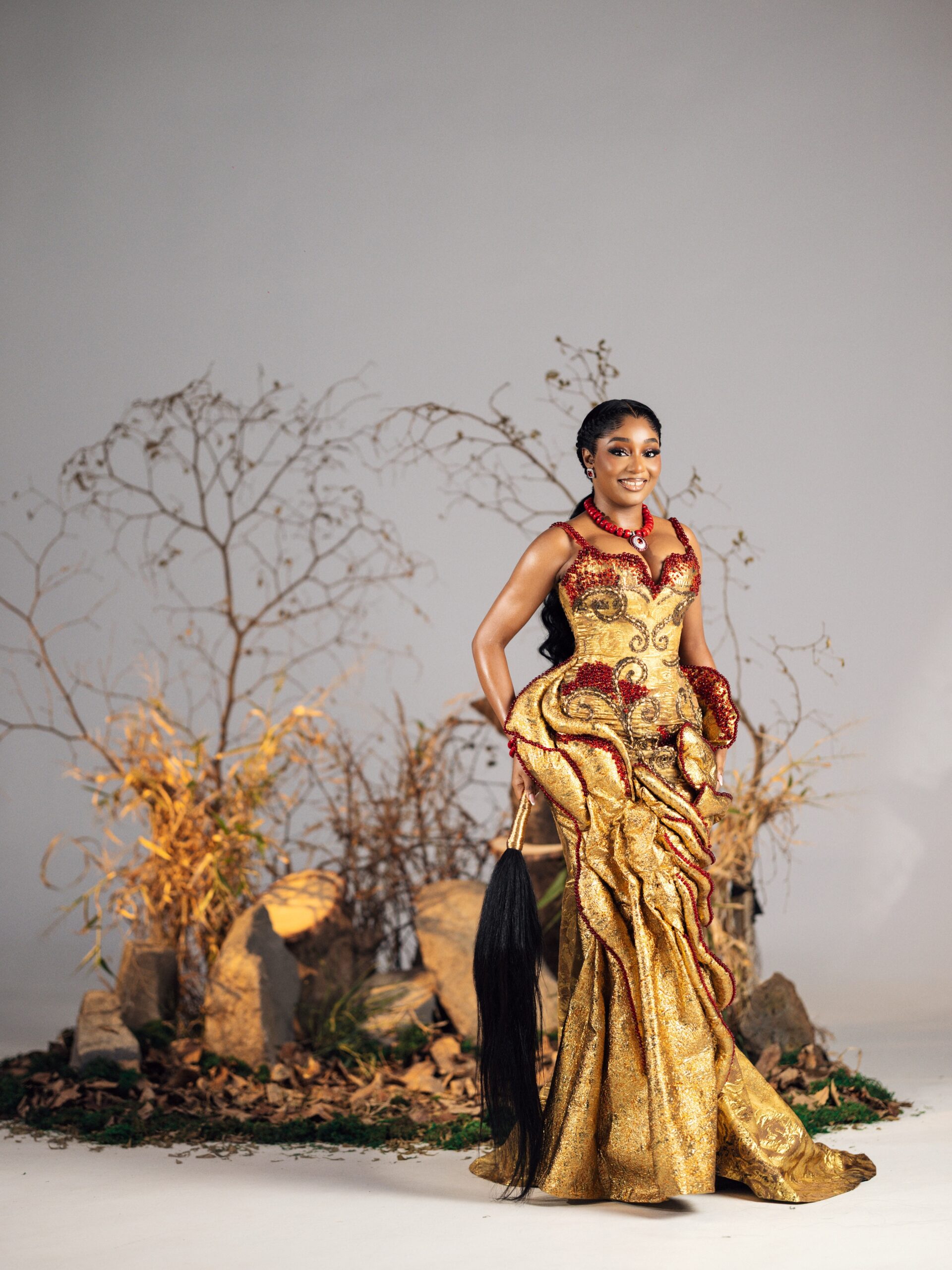 Kiky Festus wearing a custom Emagine By Bukola gold brocade corset gown embellished with ruby crystal beads and a black ukwu fly-whisk.
