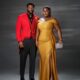 Blessing Jessica Obasi wearing a gold satin dress with a crystal Alice headband next to Stan Nze in a red tailcoat.