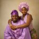 Olamide in a lilac corset halter gown hugging Kamo State wearing a lilac embroidered agbada from behind.