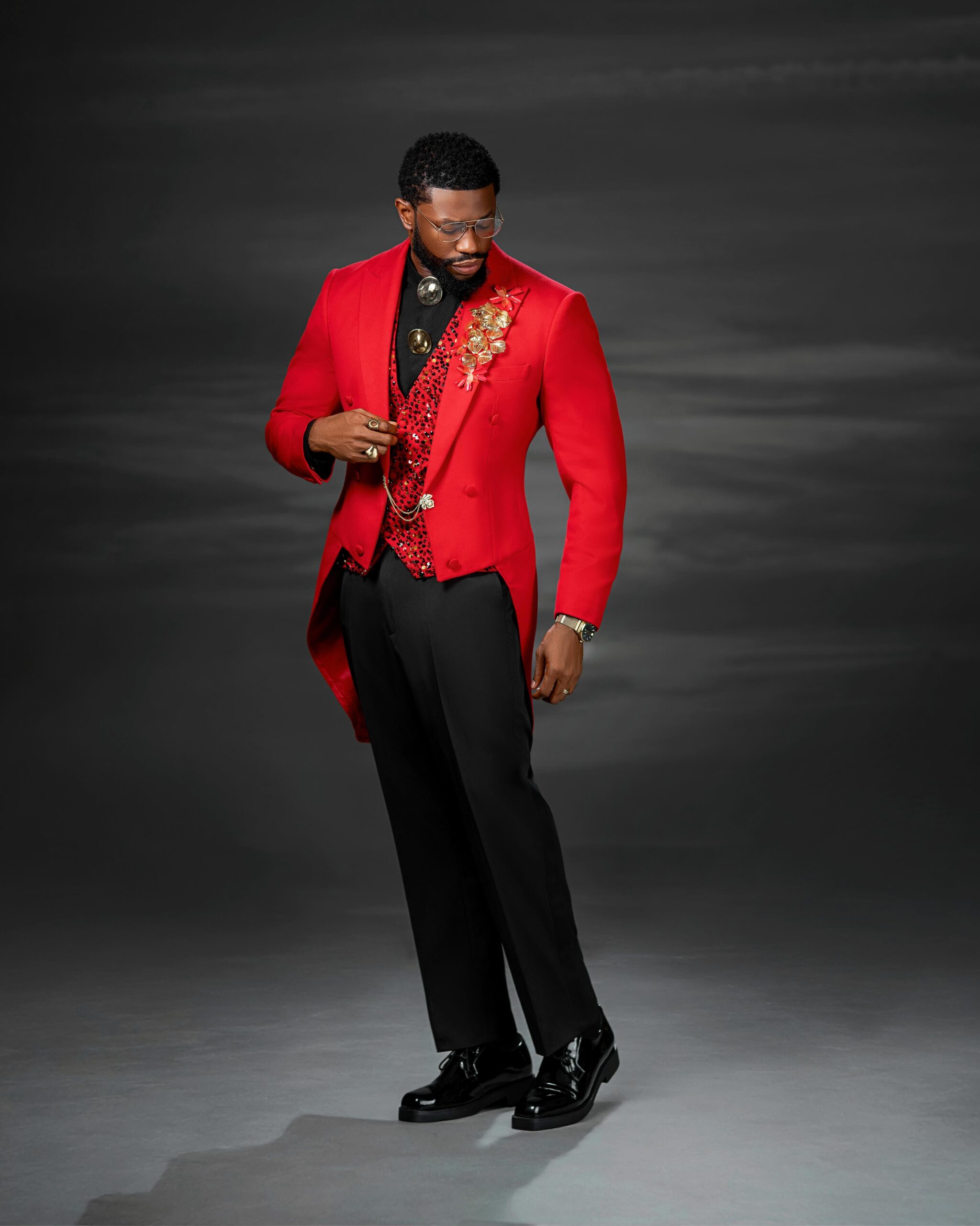 Stan Nze wearing a red double-breasted tailcoat, red sequined waistcoat, and black dress trousers for the 19 movie premiere.