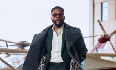 Ebuka Obi-Uchendu opening a charcoal windowpane Deji & Kola trench coat to reveal a floral silk interior lining over a green suit.