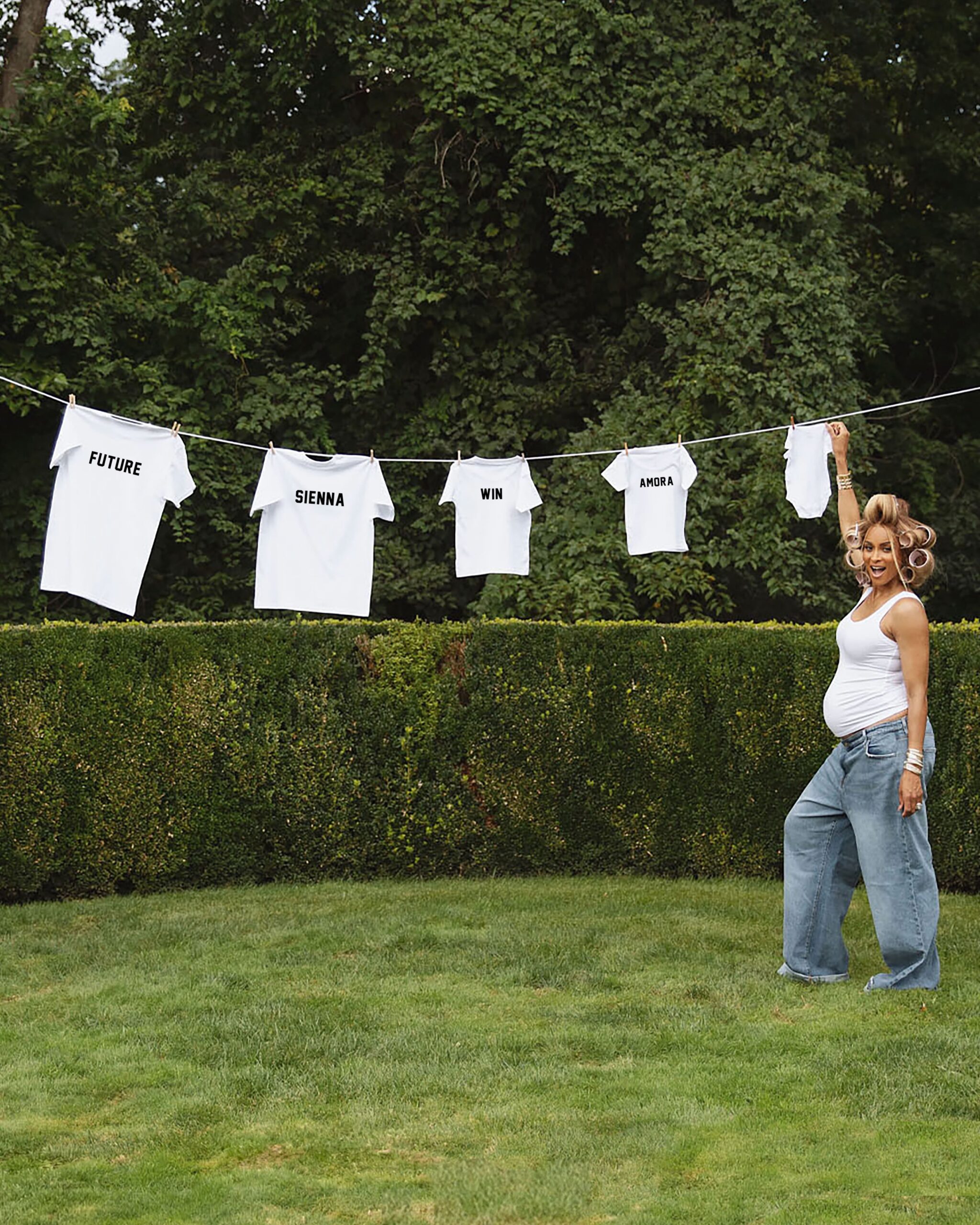 Ciara standing under a clothesline displaying t-shirts printed with her children's names Future Sienna Win Amora and a baby onesie.