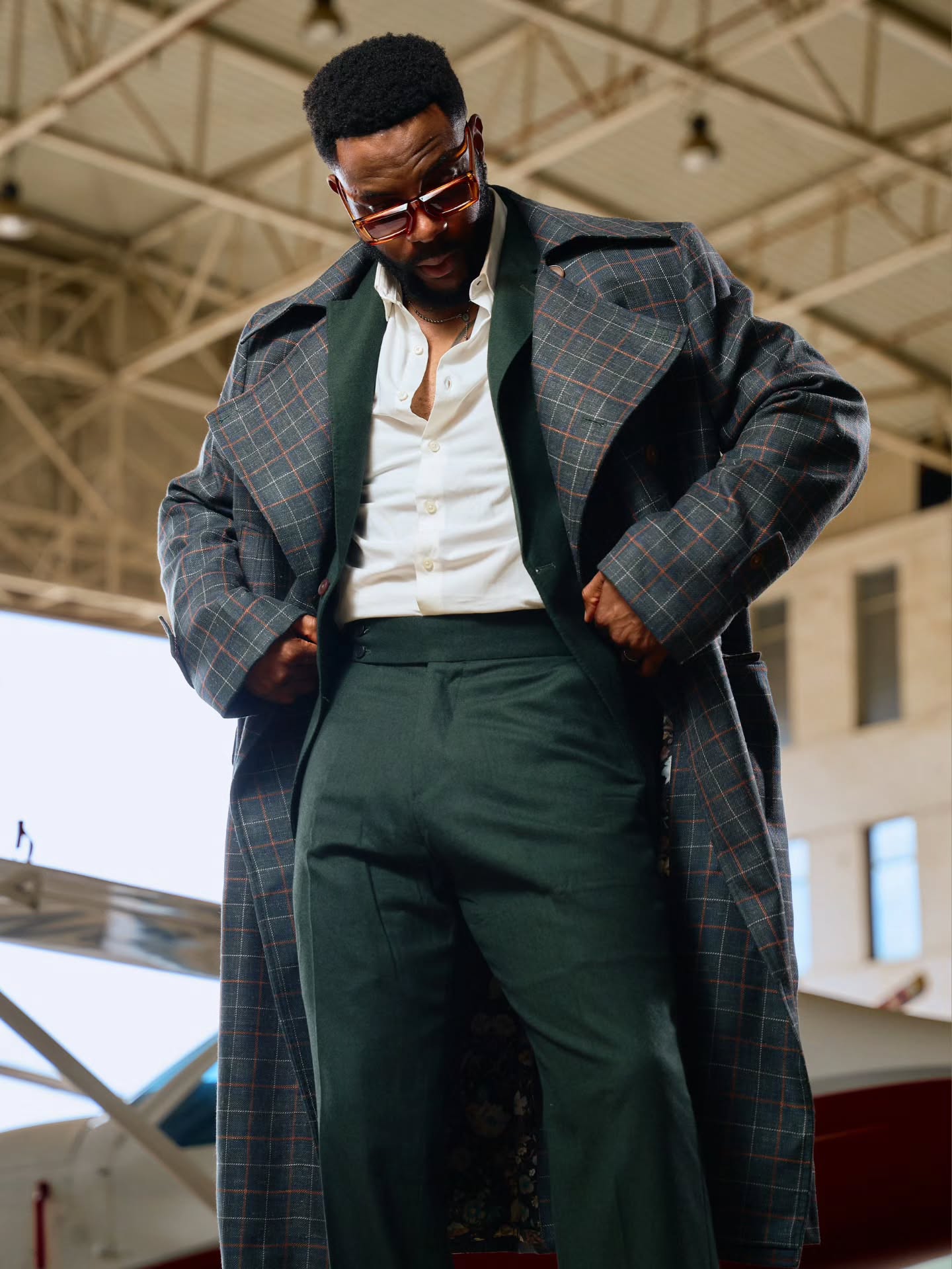 Ebuka Obi-Uchendu highlighting high-waisted green suit trousers and broad notched lapels of a Deji & Kola plaid trench coat.