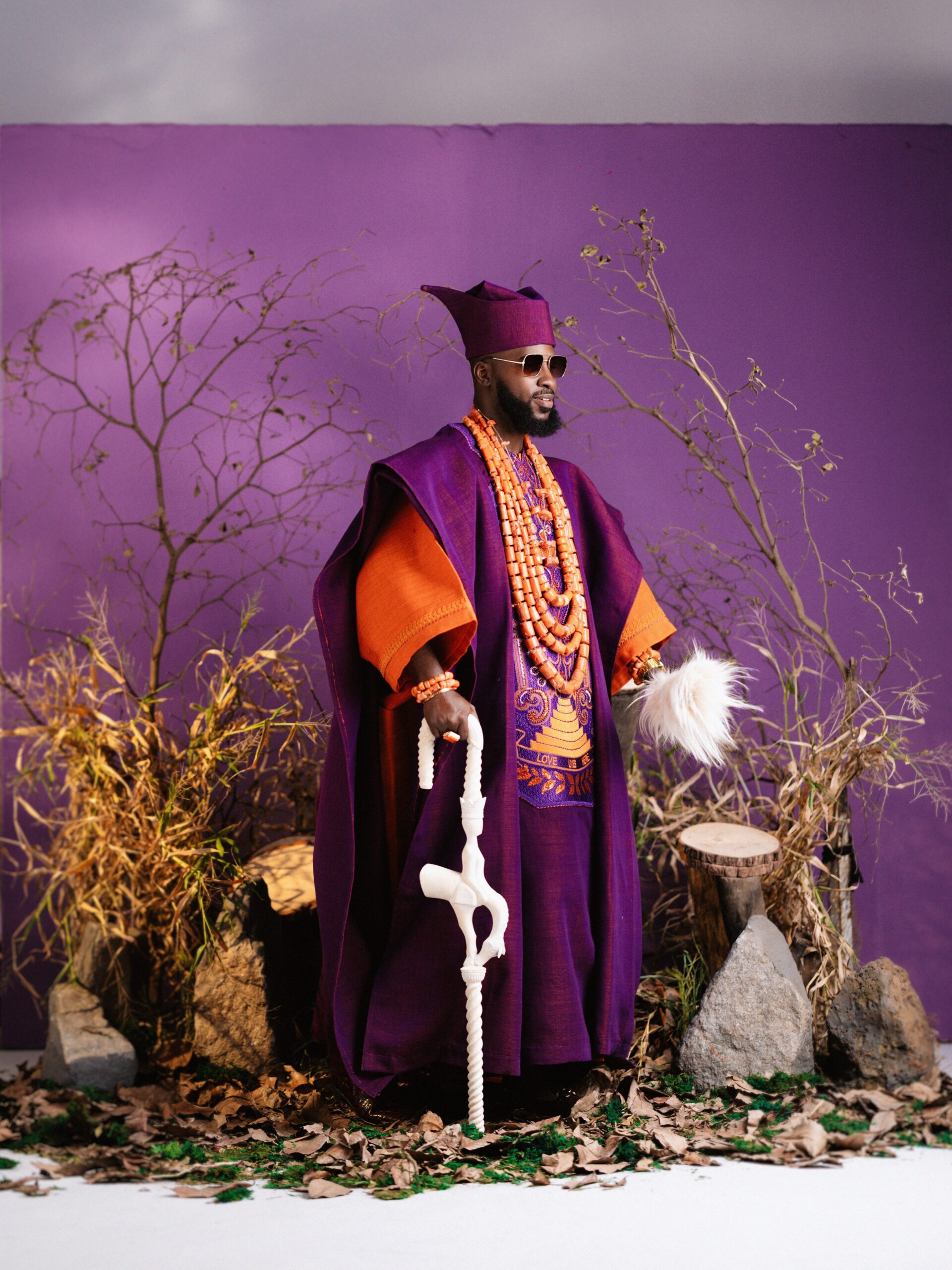 Akin Faminu in a royal purple Ugo Monye agbada over a bright orange inner tunic with multi-strand coral beads.