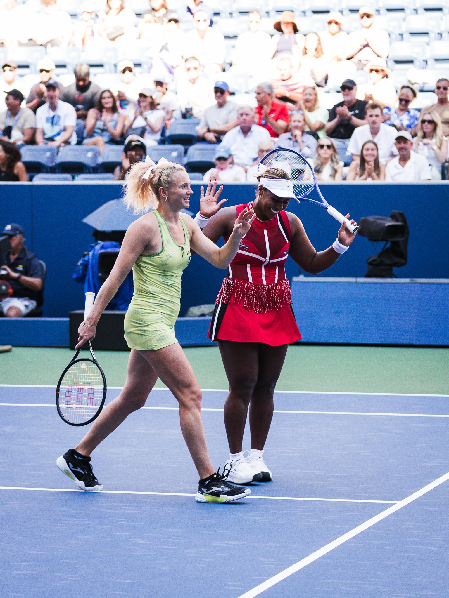 Taylor Townsend wearing a red fringe outfit high-fiving partner Katerina Siniakova on court.