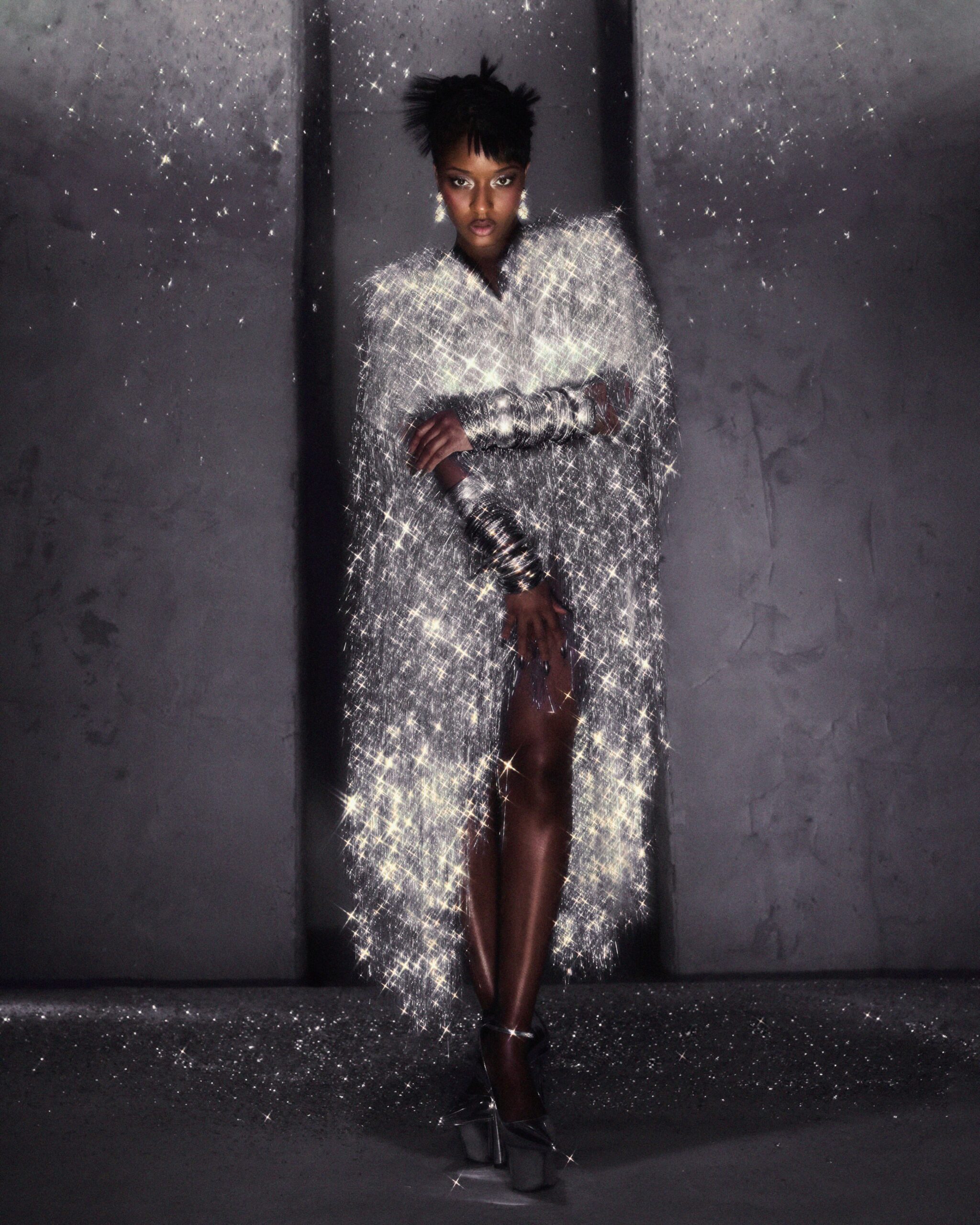 Ayra Starr in a shimmering silver tinsel cape dress with drop earrings, photographed by Fernando Tomaz for 66 GREENE Magazine.