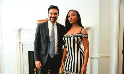 Ayra Starr in a black-and-cream striped dress standing beside Zohran Mamdani in a suit and slate-blue tie in New York.