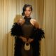 Bella Okagbue wearing a black fishnet halter gown by Dorhann by Hannah with a beaded neck, black feather boa, and gold crystal mini bag for the Akin Faminu and Kiky Festus white wedding.