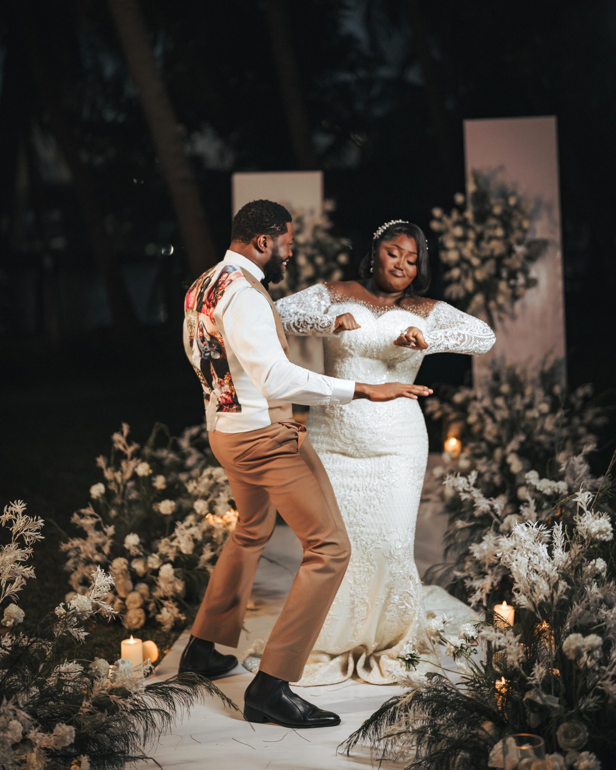 Stan Nze showing custom photo collage waistcoat back while dancing with wife Blessing Obasi Nzediegwu on flower-lined white aisle.